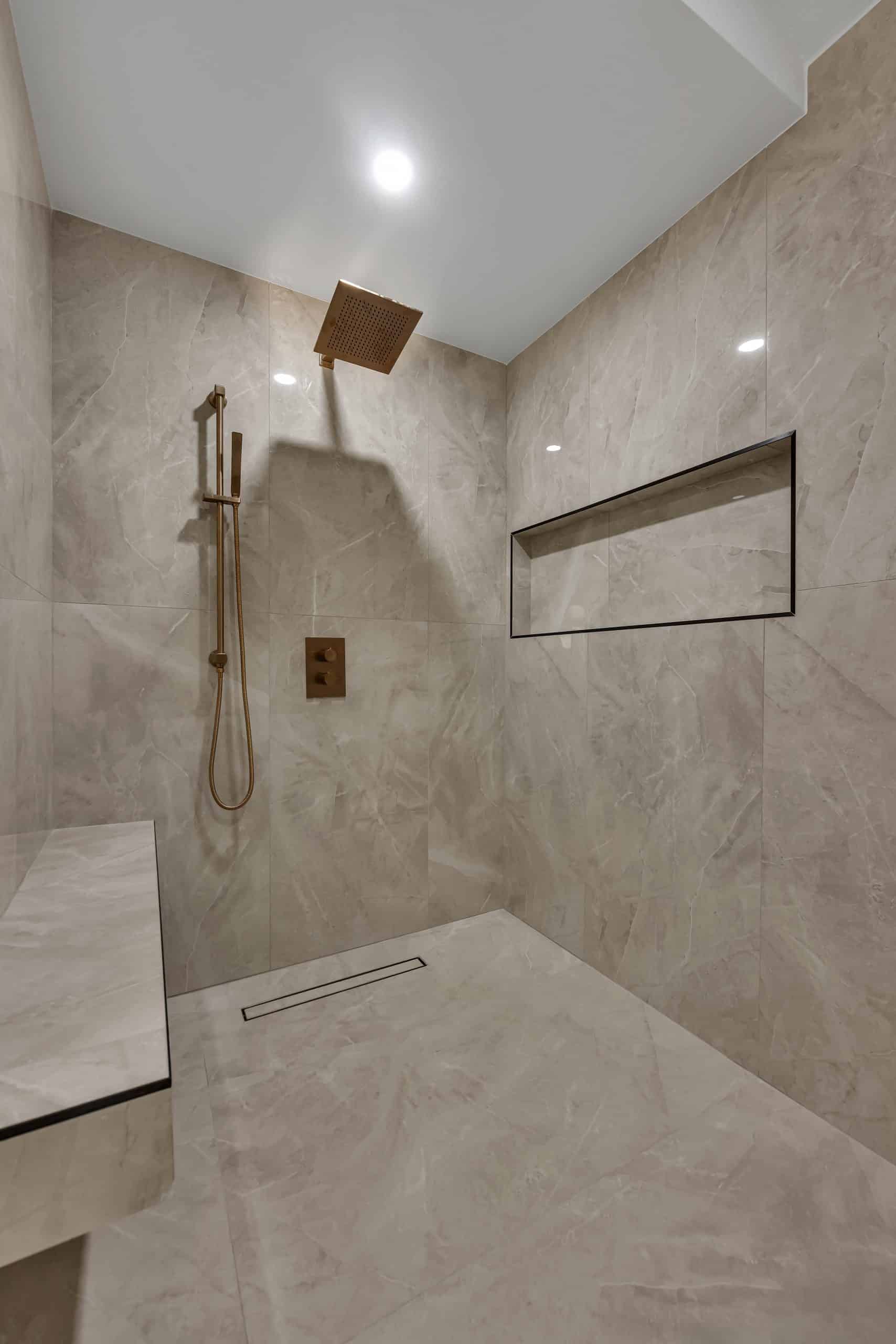 Pleasanton master bathroom — curbless walk-in shower with brushed-gold rain head, linear drain, framed niche, and bench