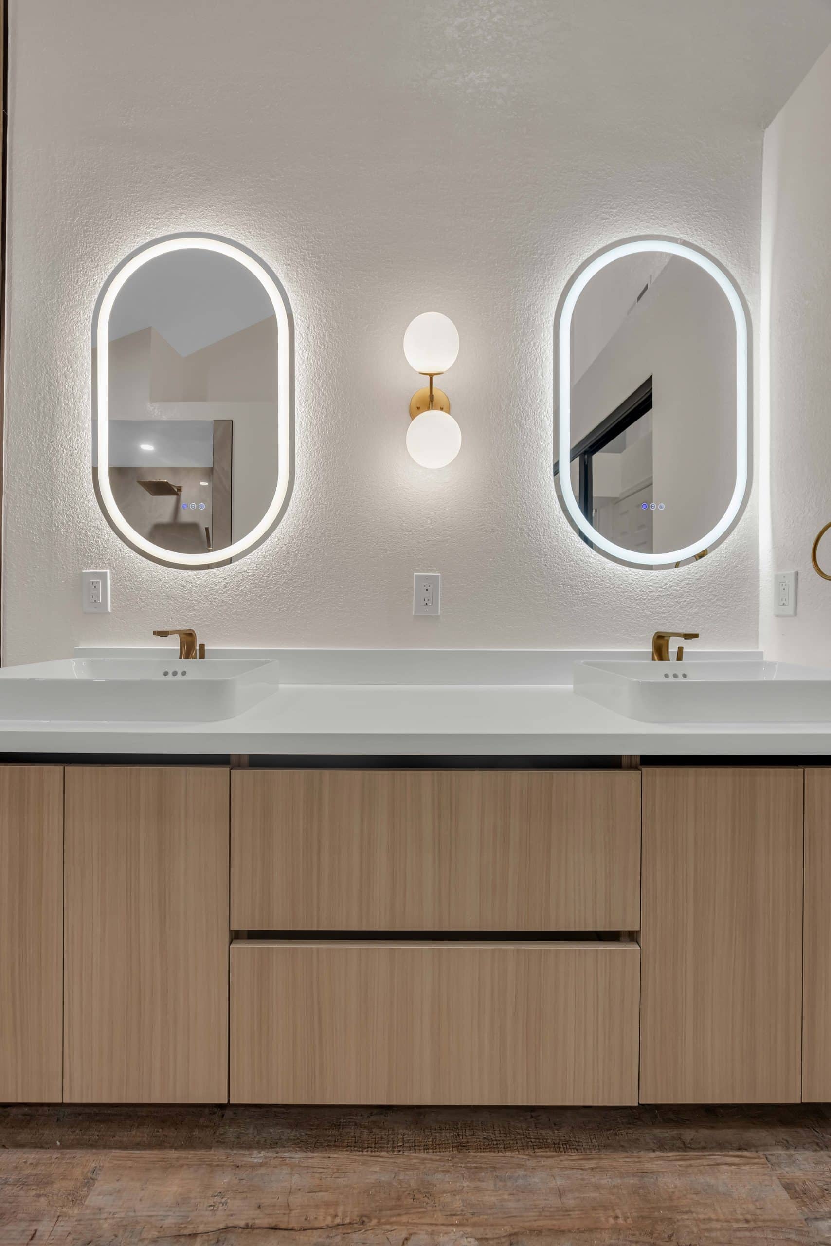 Pleasanton master bathroom — dual floating oak vanity with white vessel sinks, brushed-gold faucets, and oval LED mirrors
