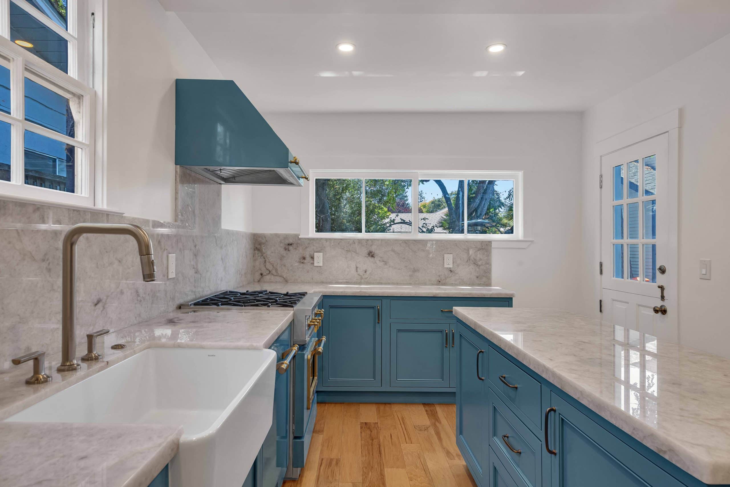 Menlo Park kitchen — white farmhouse apron sink, brass gooseneck faucet, honed marble counters, and blue Shaker cabinets