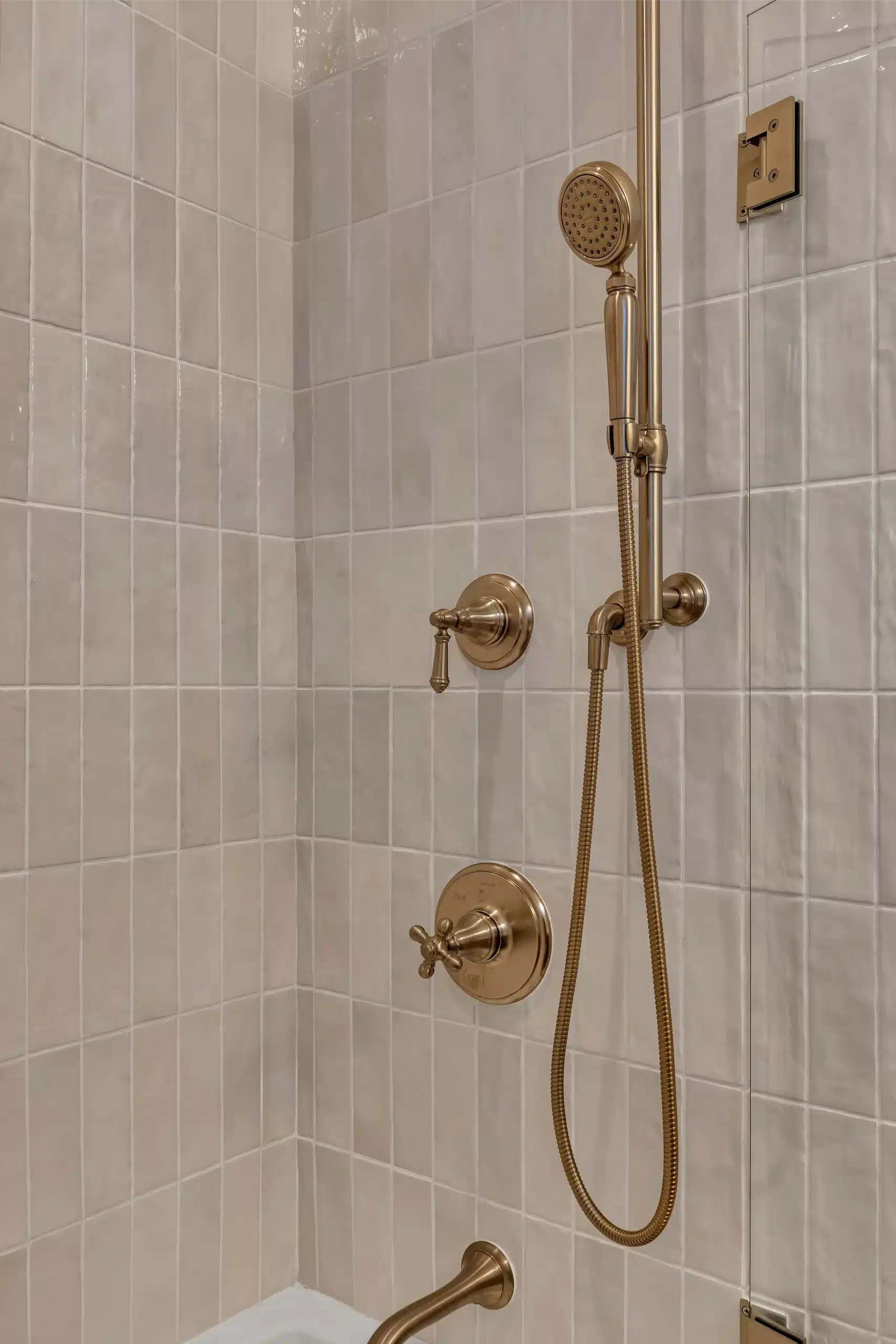 Brass shower trim with thermostatic valve and handheld on a stone-look tiled wall