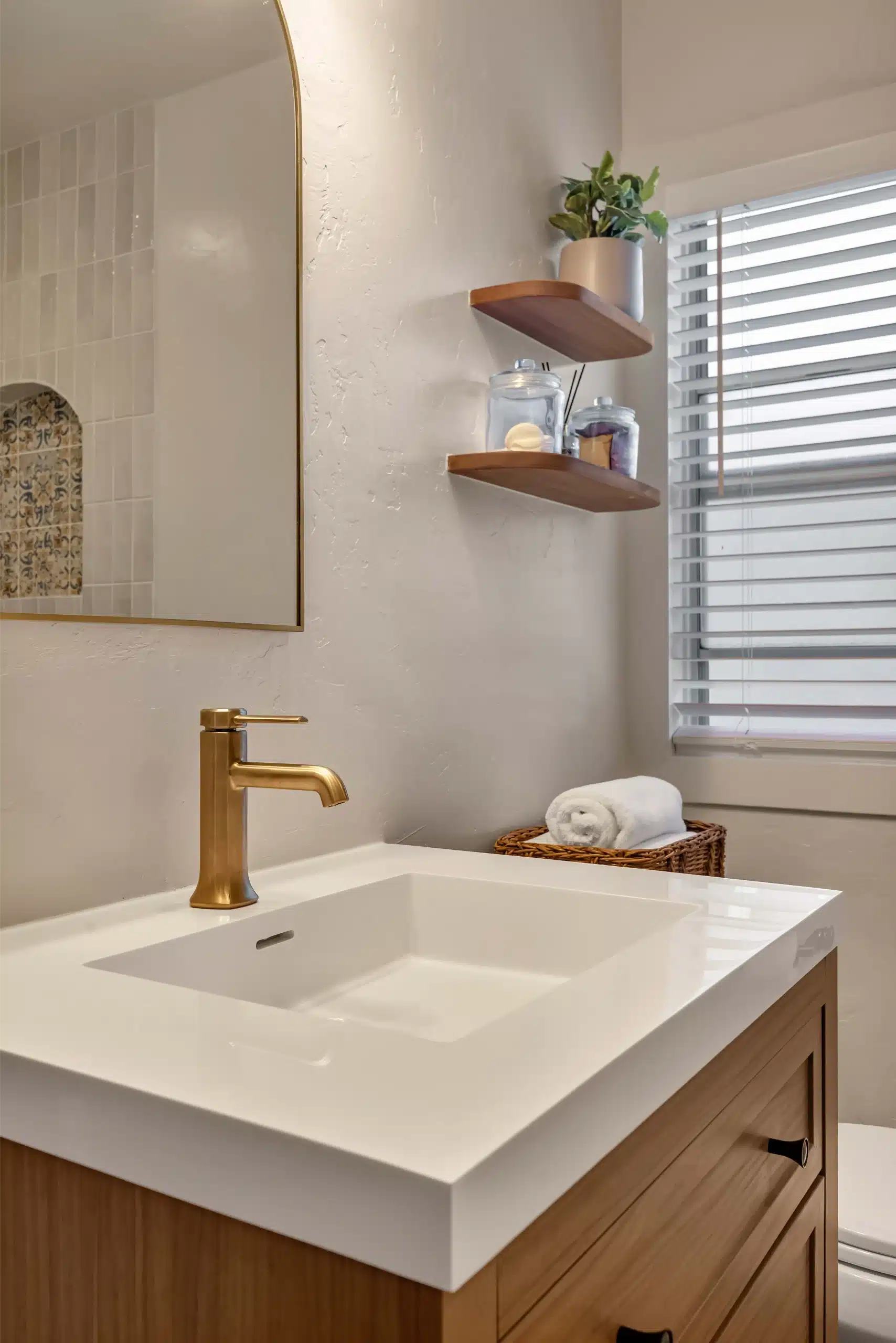 Floating oak vanity with an integrated white basin and wall-mounted brass mixer