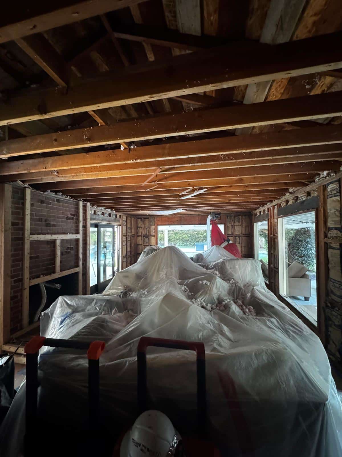 Interior stripped back during demolition, with original ceiling joists and a brick chimney exposed and remaining fixtures sheeted in plastic