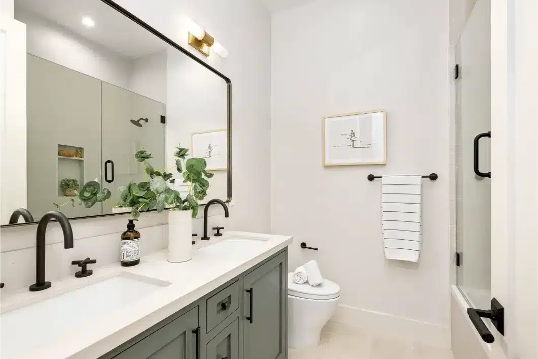 Modern bathroom with gray dual vanity, black faucets, large mirror, potted plants, and glass shower enclosure